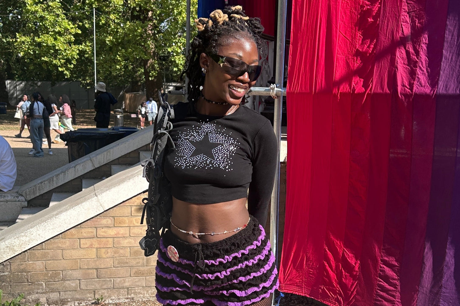 A woman in a black top and purple shorts is standing outdoors near a red and purple tent.